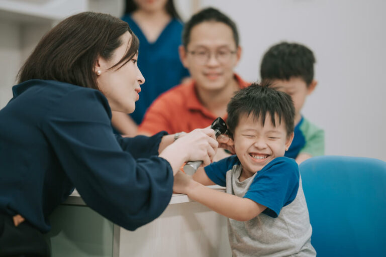 Asian Chinese female Paediatrician examining young boy ear with otoscope in her clinic.