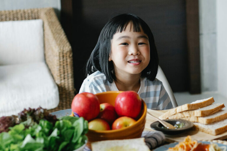 Smiling little Asian-American girl eats lunch at home.